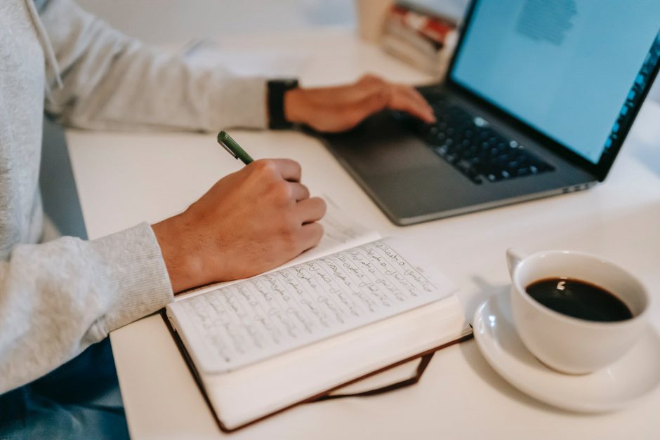 freelancer browsing laptop and taking notes in notebook during work